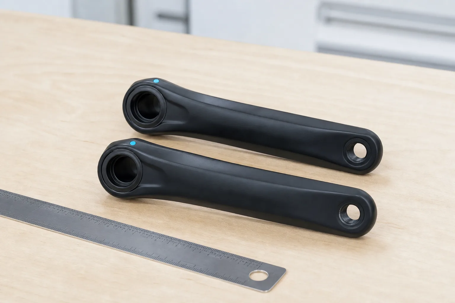 Two unbranded crank arms aligned for a centre-to-centre length comparison.